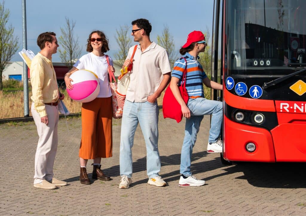 Vier Strandbesucher mit Strandausrüstung steigen in den Strandbus auf dem Weg zum Strand von Zandvoort ein.