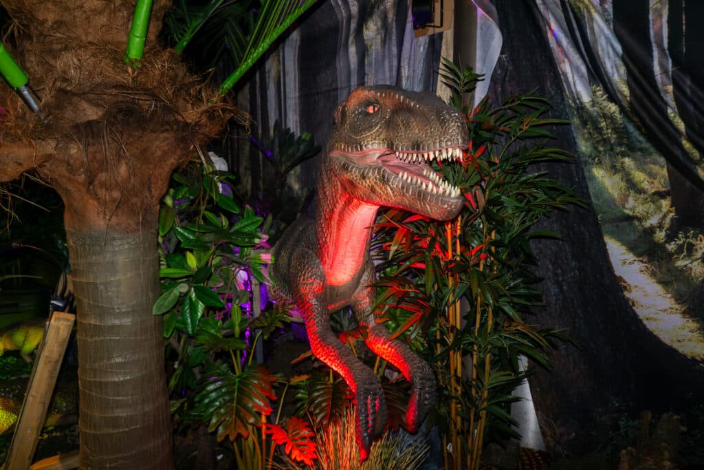 Animatronischer Velociraptor zwischen tropischen Pflanzen und Bäumen in der Indoor-Dinosaurierausstellung World of Dinos in Zandvoort.